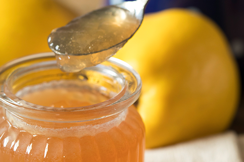 kweepeer gelei in glazen pot met op de achtergrond citroenen